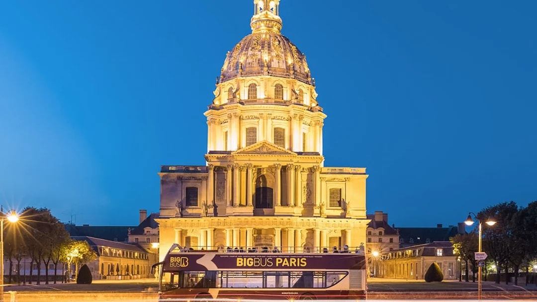 Open-top tour bus in front of Les Invalides, Paris at night.