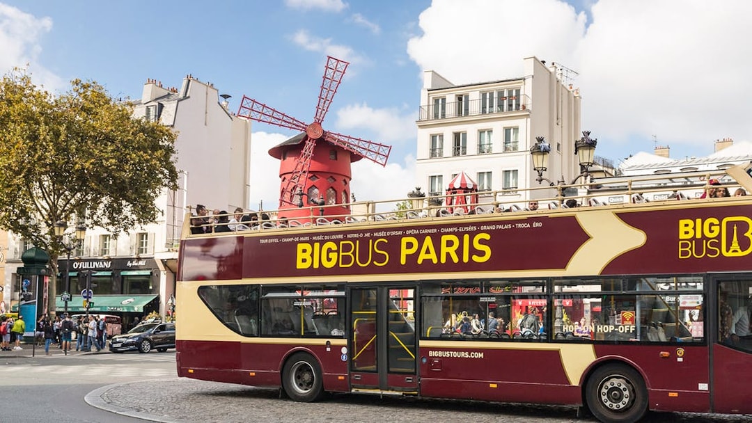 Tourists on BigBus Paris passing Moulin Rouge on hop-on-hop-off tour.