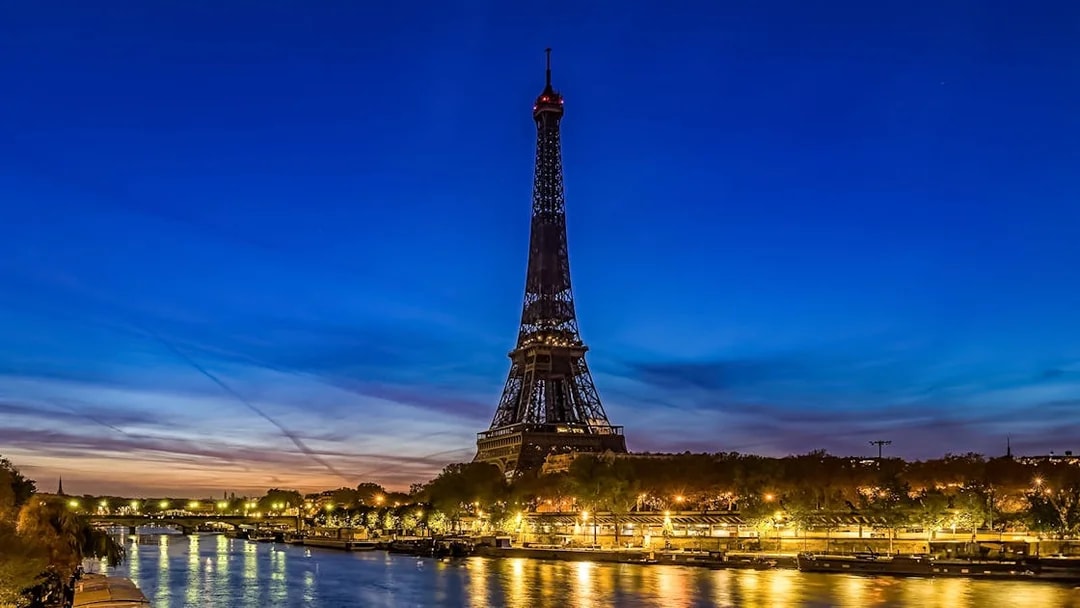 Eiffel Tower illuminated at evening with Seine River in foreground, Paris.