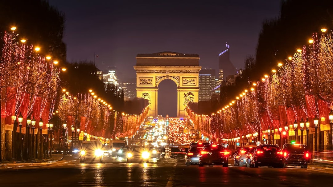 Champs-Élysées illuminated at evening with Arc de Triomphe in the background.