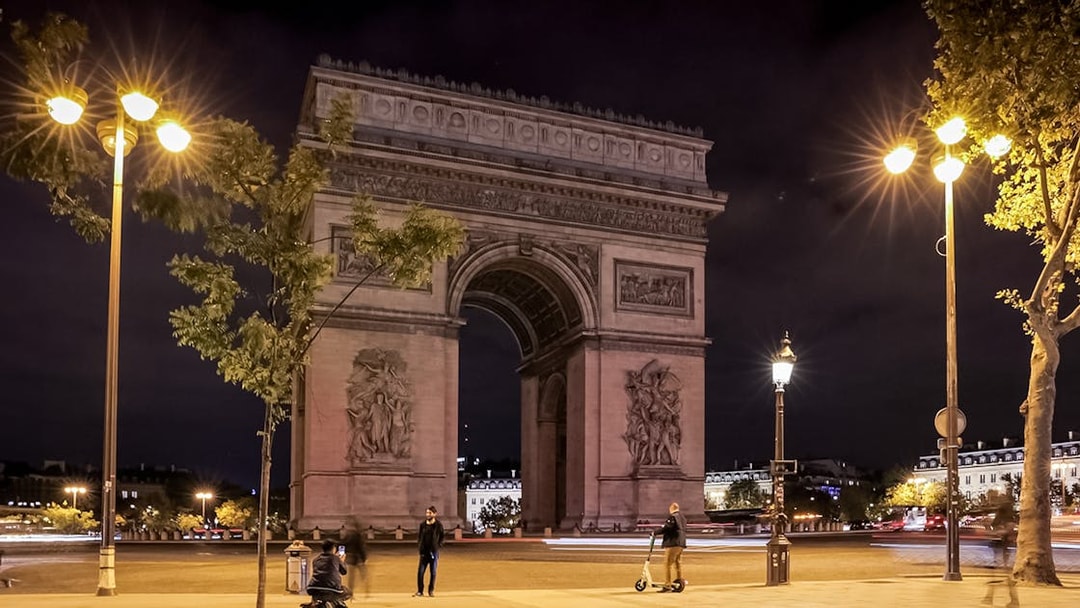 Arc de Triomphe illuminated at night with people and scooters, Paris.