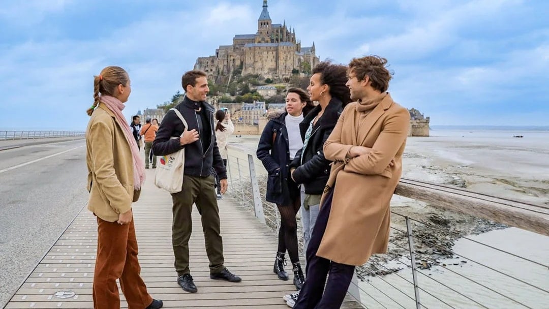 Group of tourists on a bridge with Mont Saint Michel in the background.