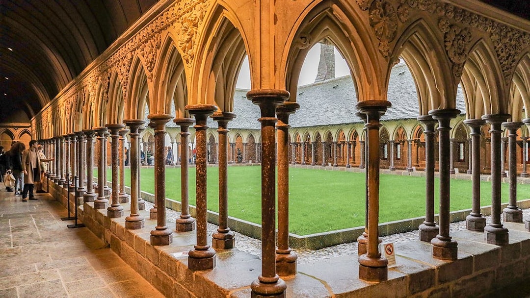 Cloister arches at Mont Saint Michel with visitors exploring the historic site.