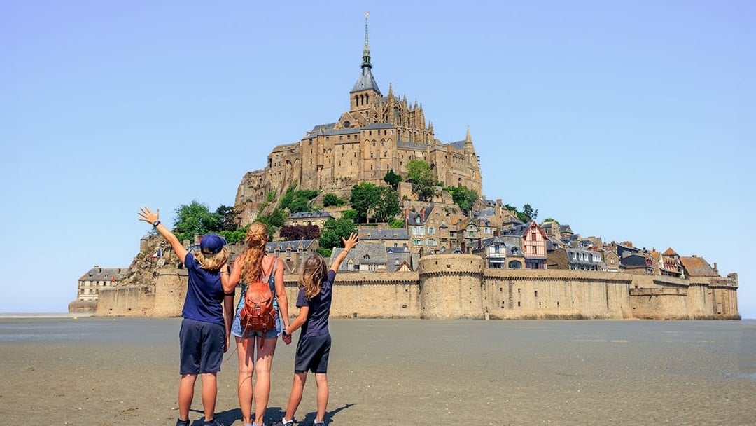 Visitors admire Mont Saint-Michel from the sandy shore, Normandy, France.