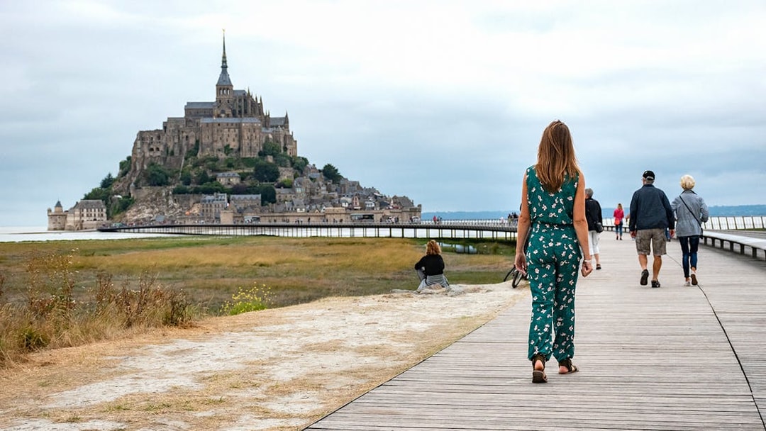 Visitors walking on a boardwalk towards Mont Saint-Michel in France.
