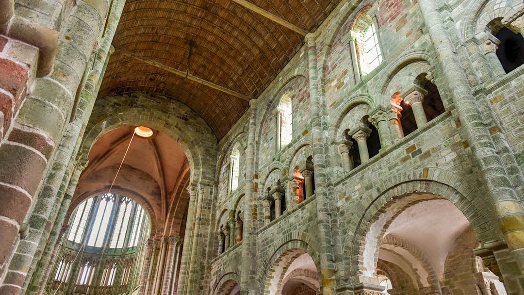 Interior of Mont Saint-Michel Abbey with stone arches and vaulted ceiling, Normandy, France.
