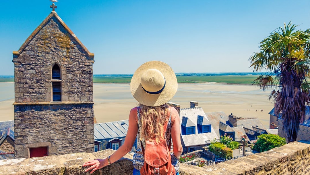 Woman overlooking Mont Saint Michel landscape with stone buildings and sandy bay.