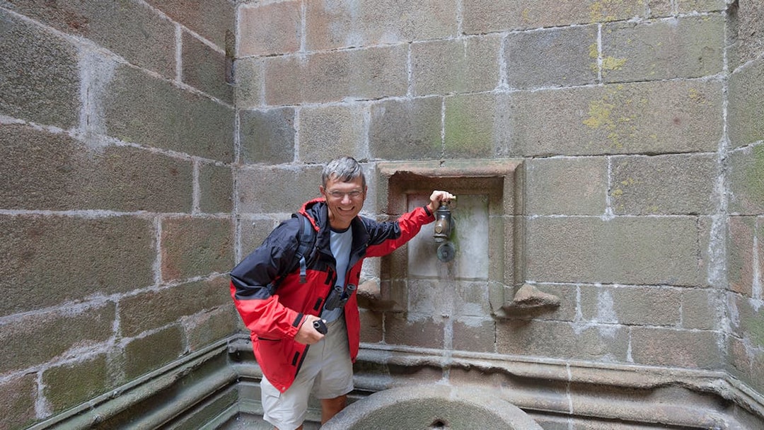 Visitor at Mont Saint-Michel fountain during Paris day trip.