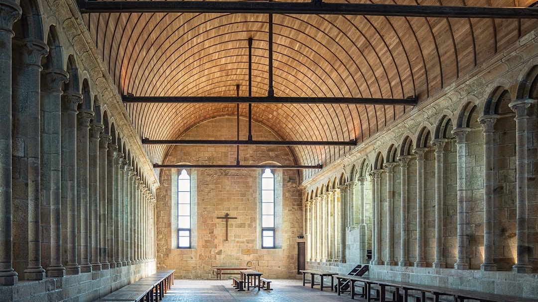 Interior of Mont St. Michel abbey with arched stone columns and wooden ceiling.