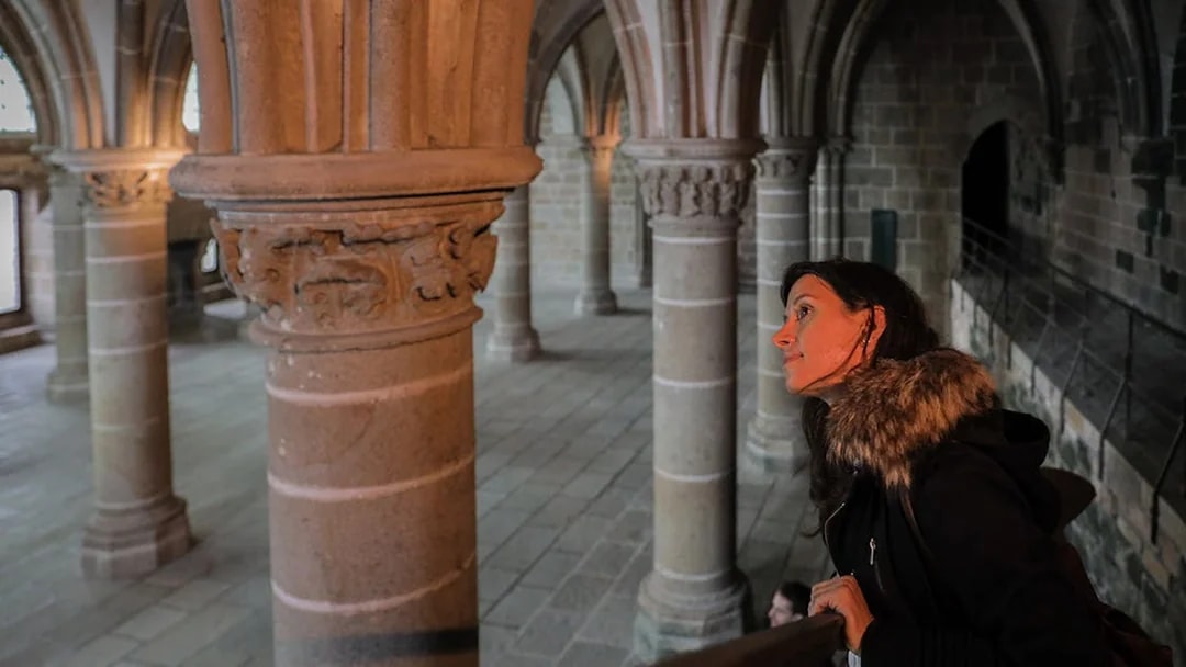 Visitor exploring the interior columns of Mont St. Michel's Abbey during a full day tour from Paris.