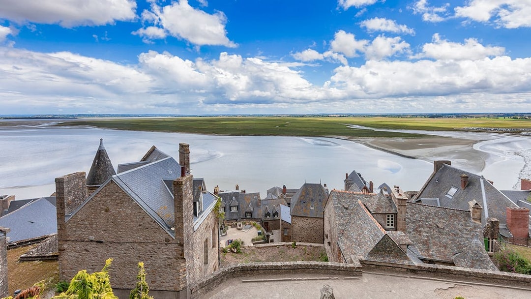 Rooftops of Mont St. Michel overlooking tidal flats and sea, seen on a full day tour from Paris.