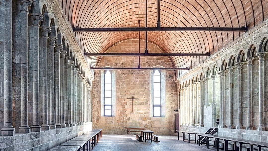 Mont-Saint-Michel Abbey interior with stone columns and wooden ceiling.