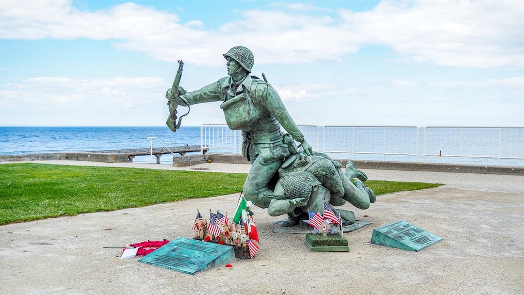 Statue of soldiers at Normandy D-Day Beach with flags and memorial plaques.