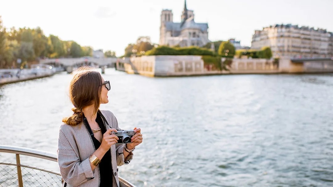 Person holding a camera on a Seine River cruise with Notre-Dame Cathedral in the background.