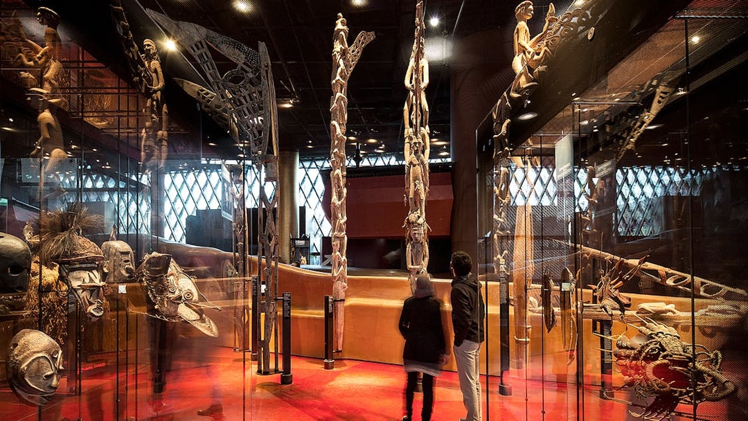Quai Branly Museum interior with visitors viewing indigenous art displays, Paris.