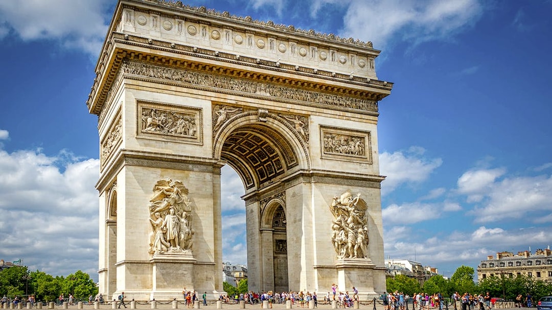 Arc De Triomphe with sculptures and tourists in Paris, France.