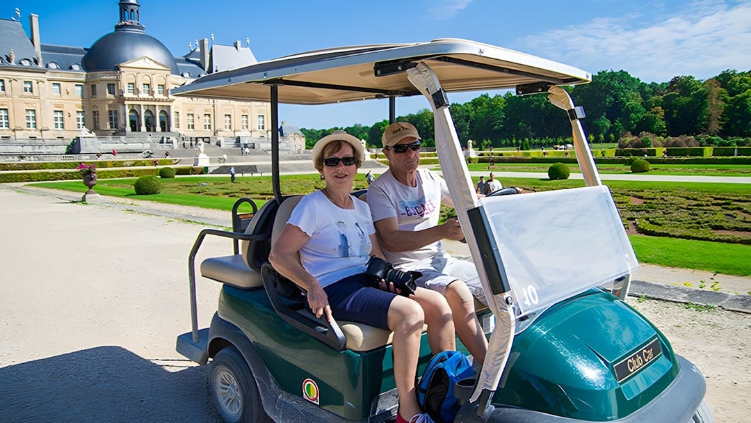 Visitors in a golf cart at Vaux-le-Vicomte, France, with the château in the background.