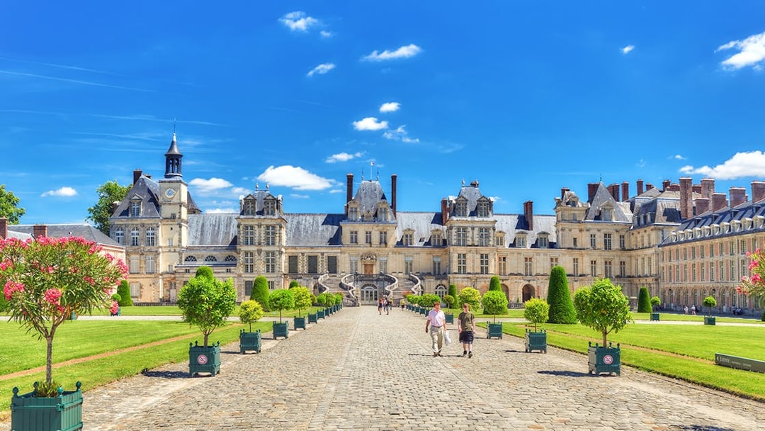 Palace of Fontainebleau courtyard with visitors walking on cobblestone path.