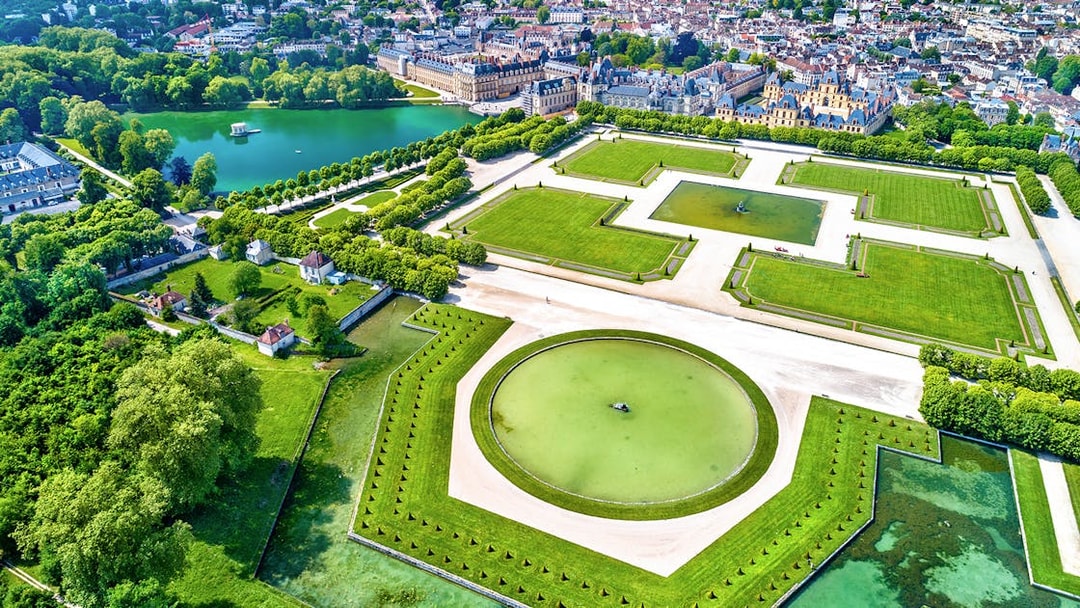 Aerial view of the Palace of Fontainebleau Gardens with geometric lawns and a central pond.