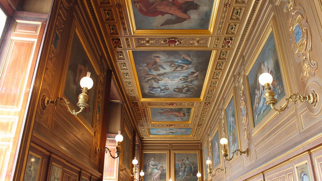 Château de Fontainebleau ornate hallway with detailed ceiling paintings and wall sconces.