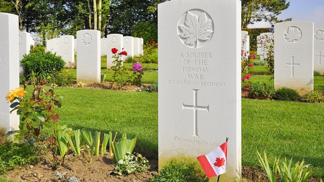Canadian war graves with flags at Normandy cemetery, France.
