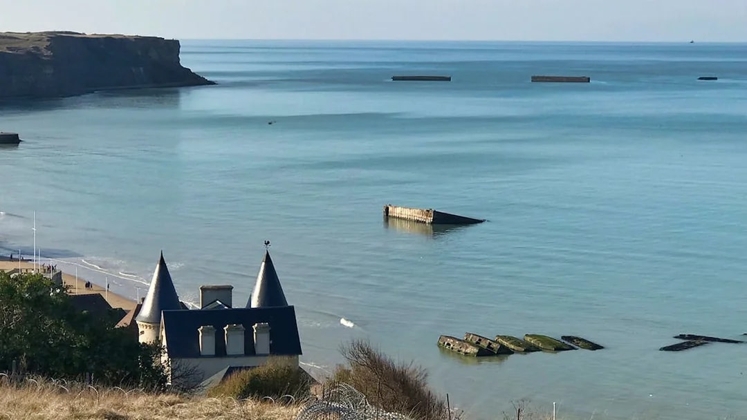 Normandy D-Day landing beach with remnants of Mulberry Harbor in the sea.