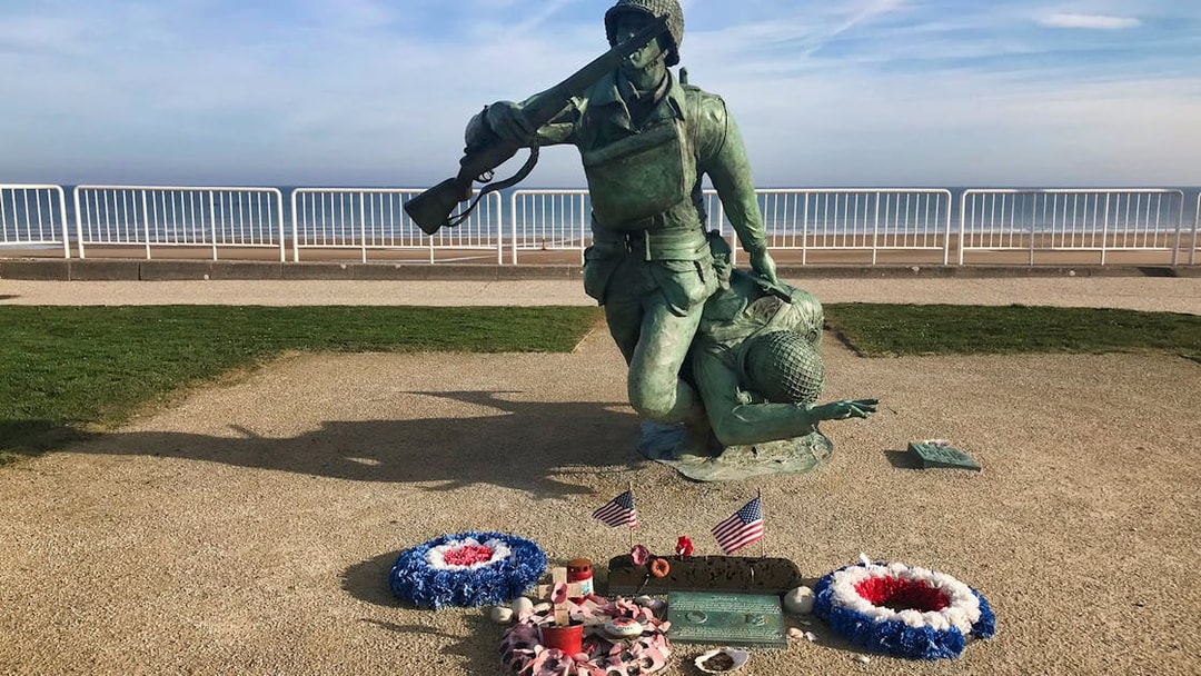 Normandy D-Day memorial statue with wreaths and flags at Omaha Beach.