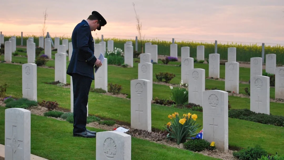 Man in uniform paying respects at Normandy D-Day cemetery at sunset.