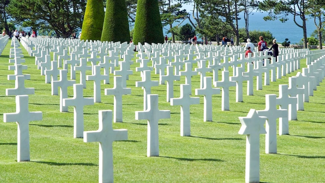 Rows of white crosses at Normandy American Cemetery, France, with visitors walking among them.