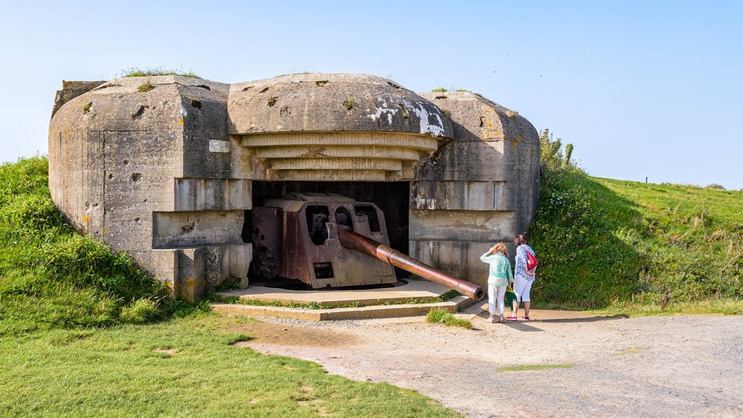 WWII Normandy bunker with tourists exploring, part of D-Day Beaches tour from Paris.