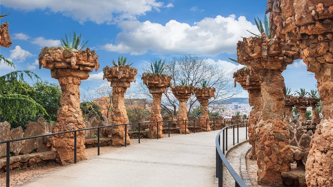 Stone columns with plants along a pathway in Park Güell, Barcelona.