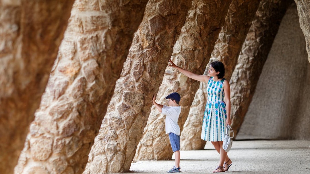 Mother and son exploring stone columns in Park Guell, Barcelona.