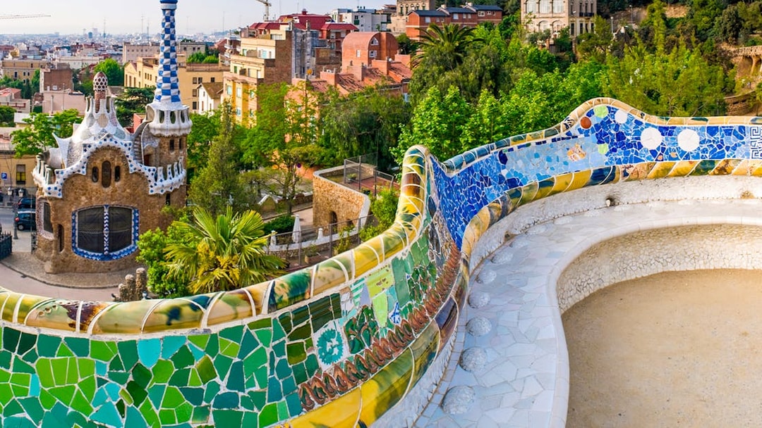 Serpentine Bench with mosaic tiles in Parc Guell, Barcelona, overlooking cityscape.