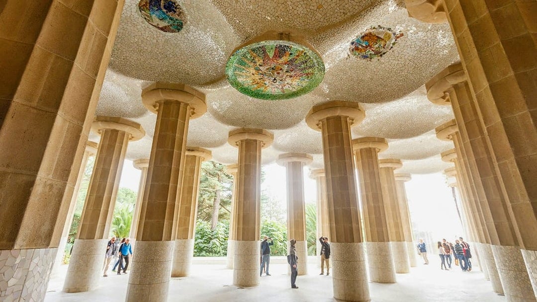 Tourists exploring the mosaic ceiling and columns at Park Guell, Barcelona.
