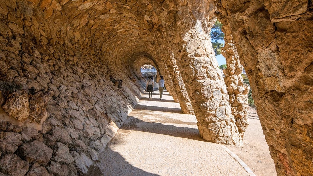 Visitors walking through stone arches in Park Güell, Barcelona.