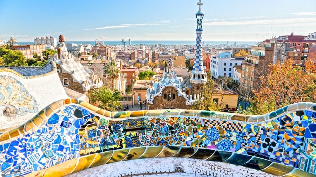 Panoramic view of Park Güell's colorful mosaic terrace overlooking Barcelona.