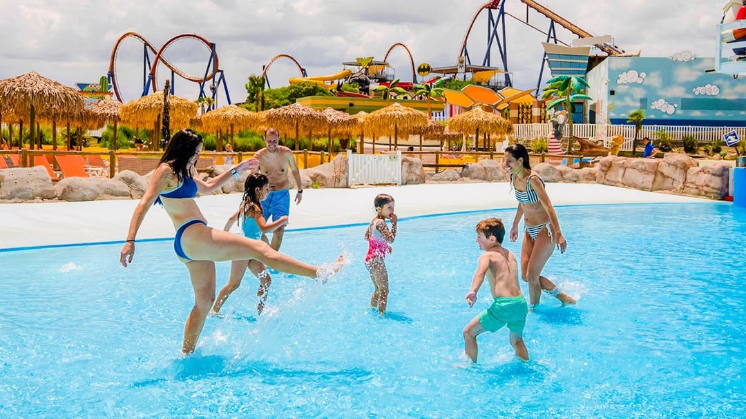 Families enjoying the wave pool at Parque Warner Beach with roller coasters in the background.
