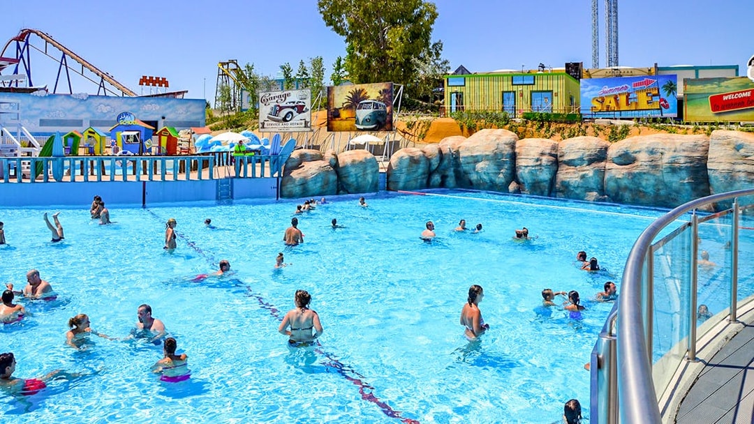 Visitors enjoying the wave pool at Parque Warner Beach, Madrid with roller coasters in the background.