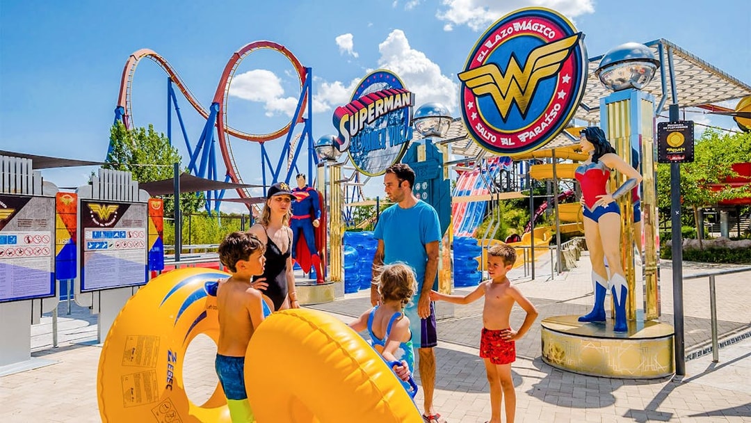 Parque Warner Madrid entrance with Superman and Wonder Woman statues, vibrant theme park atmosphere.