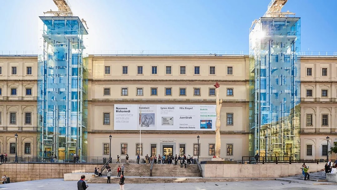 Reina Sofia Museum entrance with glass elevators and visitors in Madrid.