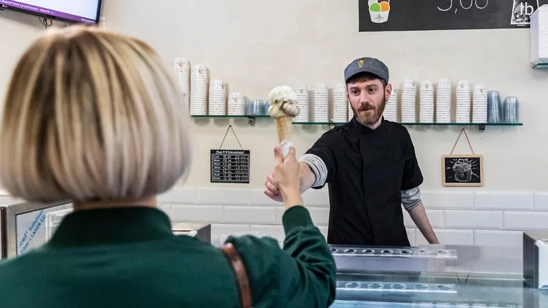 Gelato server handing cone to customer in Trastevere, Rome.