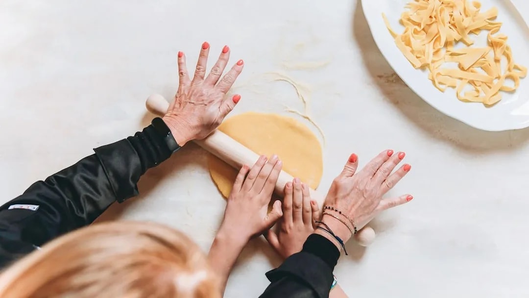 Hands rolling fresh pasta dough in a cooking class.