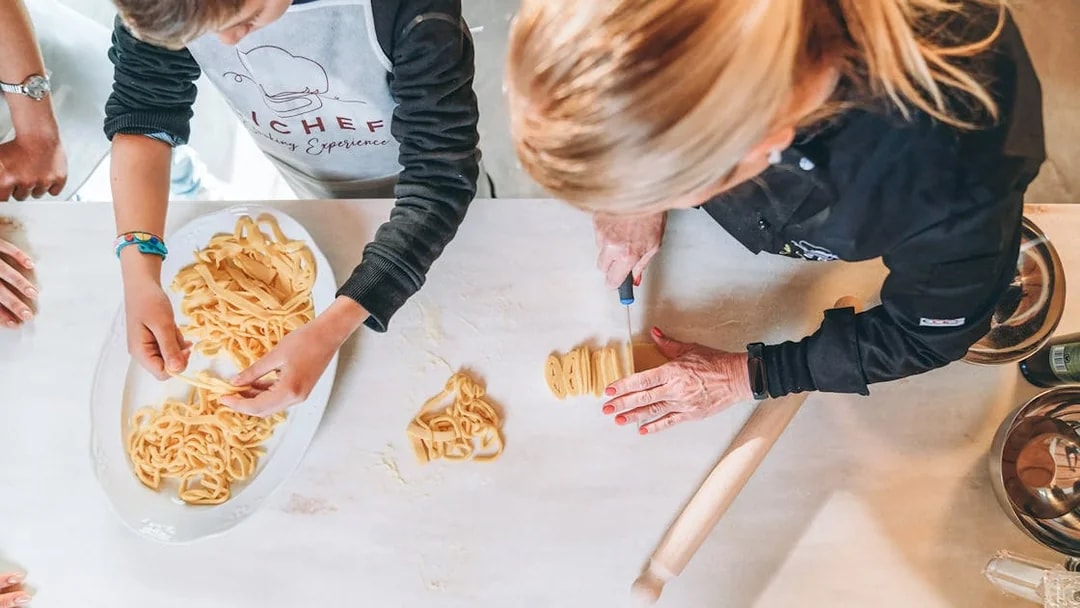 Making fresh pasta in a cooking class with a chef and participant.