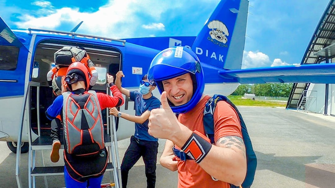 Tourists boarding a skydive plane, one giving a thumbs up, at a dropzone.