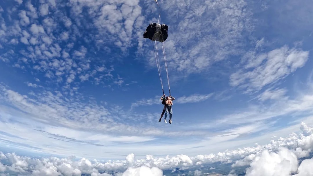 Tourist tandem skydiving with parachute over scenic landscape.