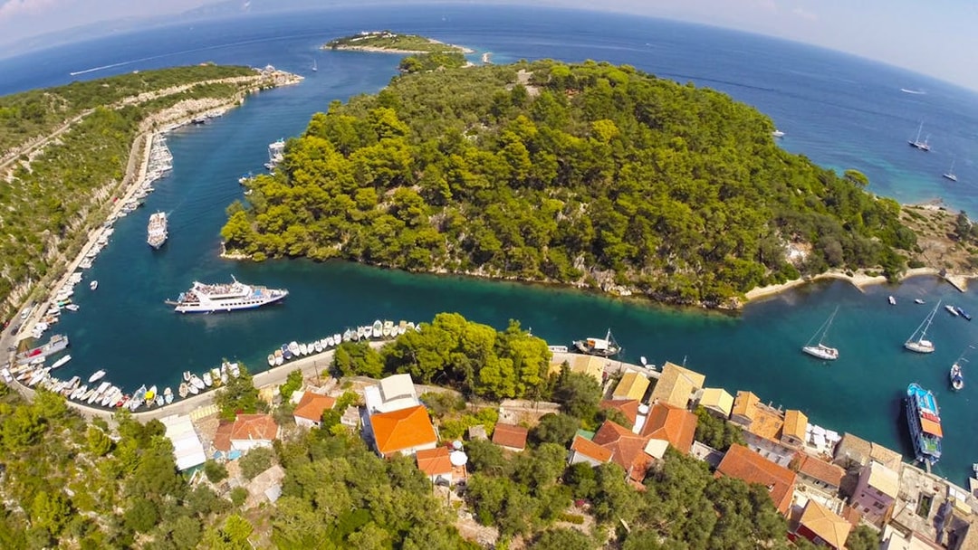 Cruise ship navigating narrow channel near Paxos island, Greece, surrounded by lush greenery and clear blue waters.