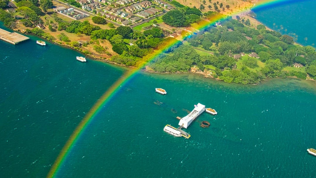 Aerial view of Arizona Memorial at Pearl Harbor with a rainbow over the water.