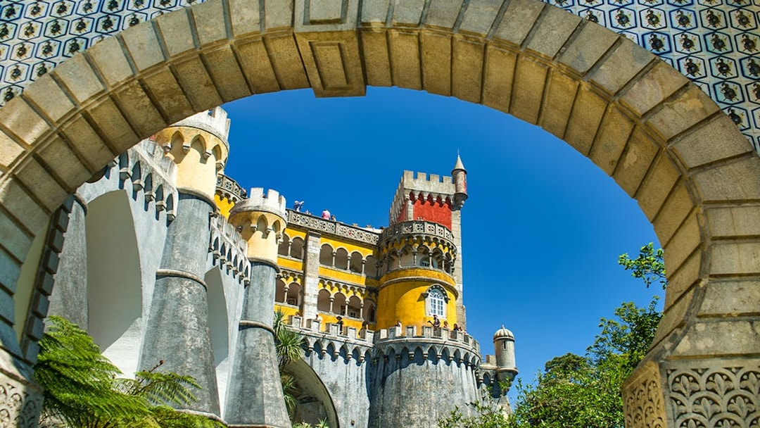 Pena Palace colorful facade viewed through stone archway, Sintra, Portugal.