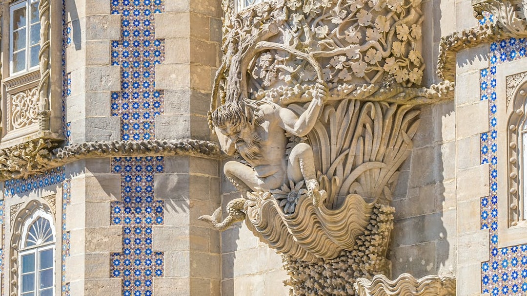 Facade detail of Pena Palace in Sintra, Portugal, featuring intricate stone carvings and blue tilework.