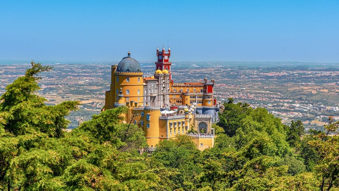 Pena Palace in Lisbon surrounded by lush greenery and overlooking the cityscape.